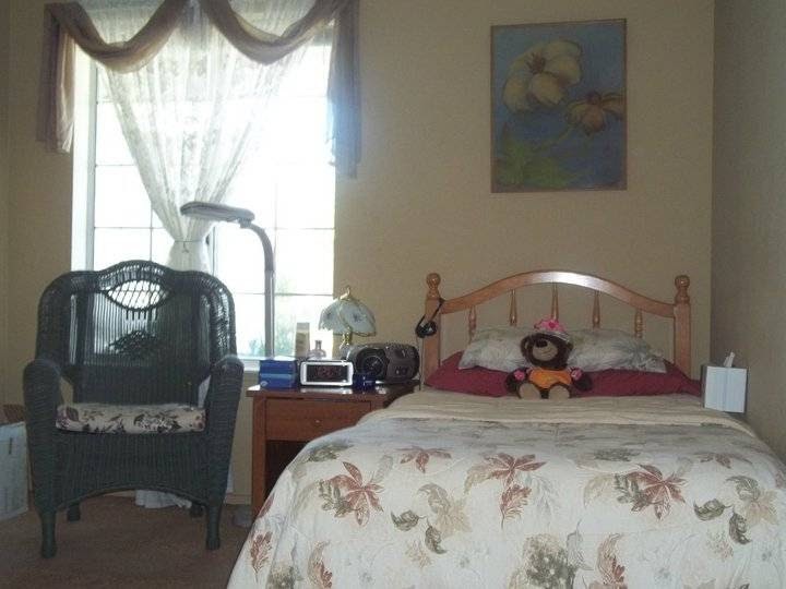 A cozy bedroom with a neatly made bed, a bedside table with a lamp, and a chair by the window.