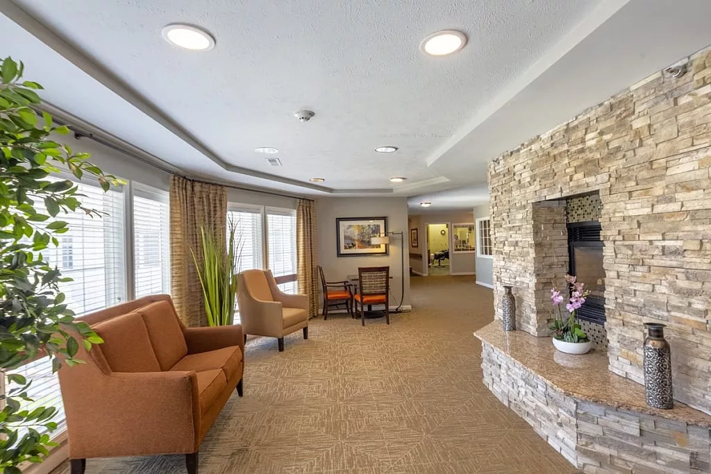 A cozy lounge area featuring comfortable seating and a stone fireplace, with ample natural light from large windows.
