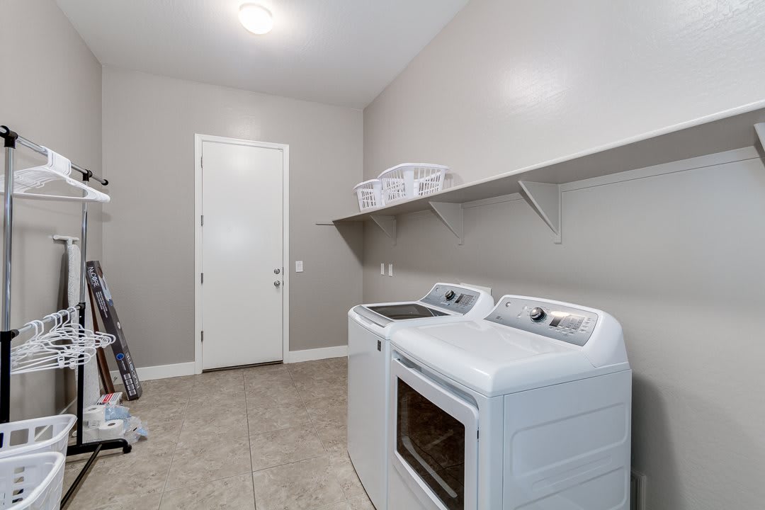A clean and modern laundry room with a washer, dryer, and shelving.