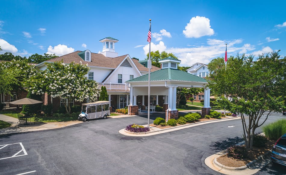 A building entrance with landscaped surroundings and a vehicle parked nearby under a blue sky.