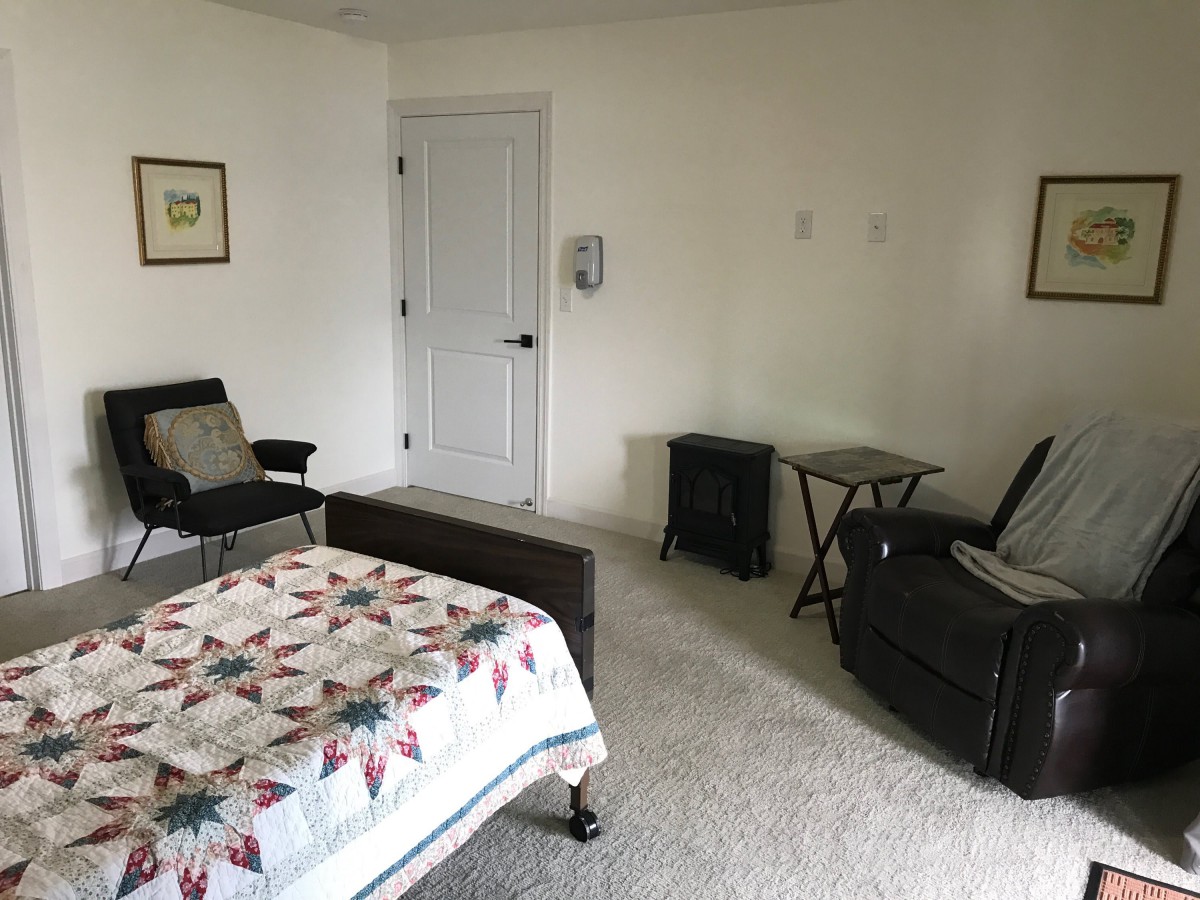 A minimalist bedroom with a quilt-covered bed, chairs, and small tables.
