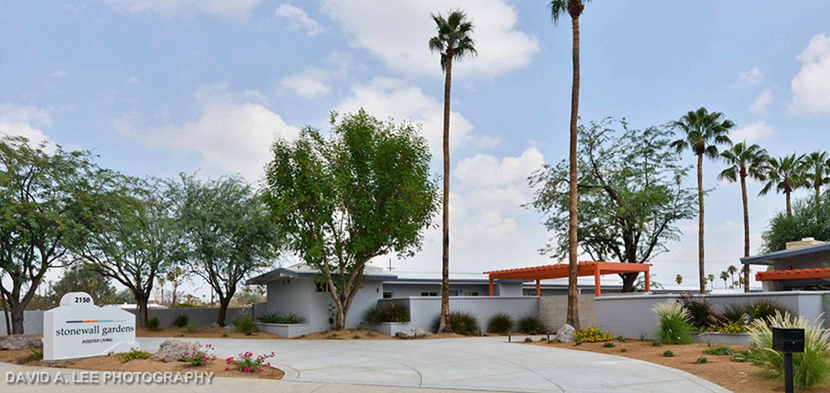 A mid-century modern house with palm trees and a cloudy sky backdrop.