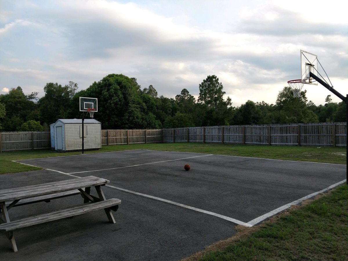 An outdoor basketball court with a bench and a basketball hoop under a cloudy sky.