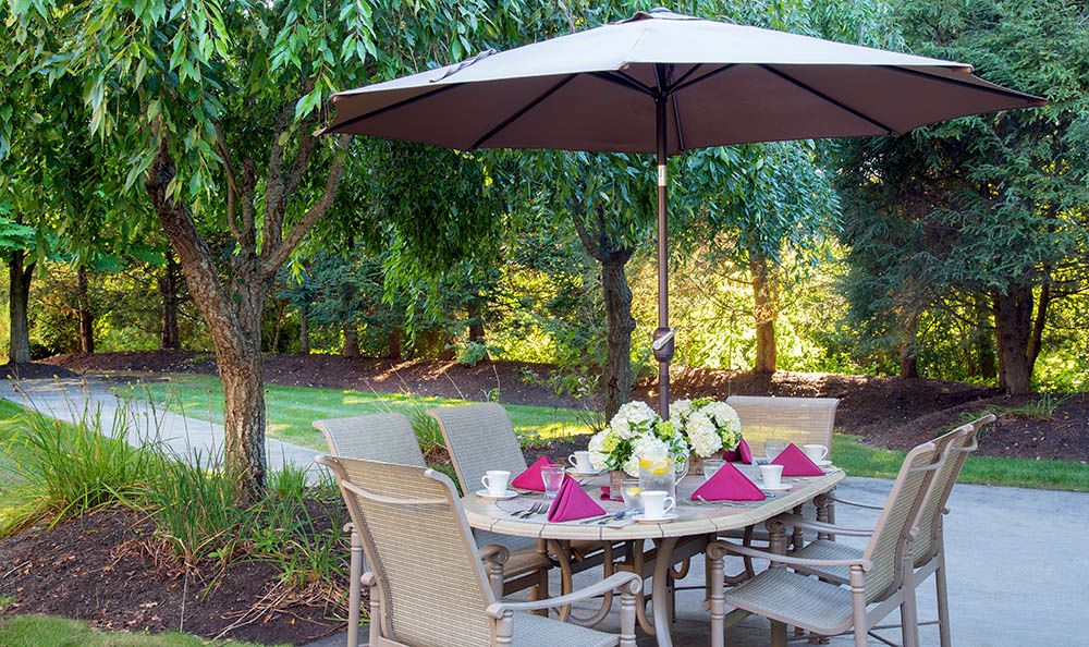 A beautifully set outdoor patio table under an umbrella, surrounded by lush greenery.