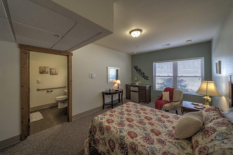 A cozy bedroom with a bed, armchair, and lamp near a window.