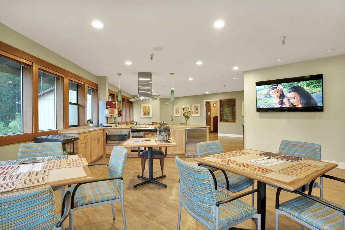 A modern kitchen and dining area featuring wood flooring, tables with chairs, and a television on the wall.