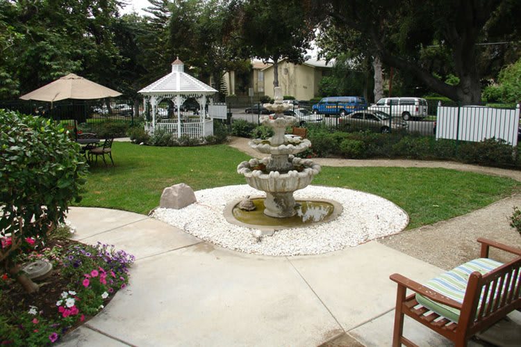 A scenic garden with a central fountain and a white gazebo surrounded by lush greenery.