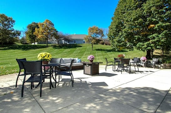 A sunny outdoor patio with seating overlooking a lush green lawn and trees.