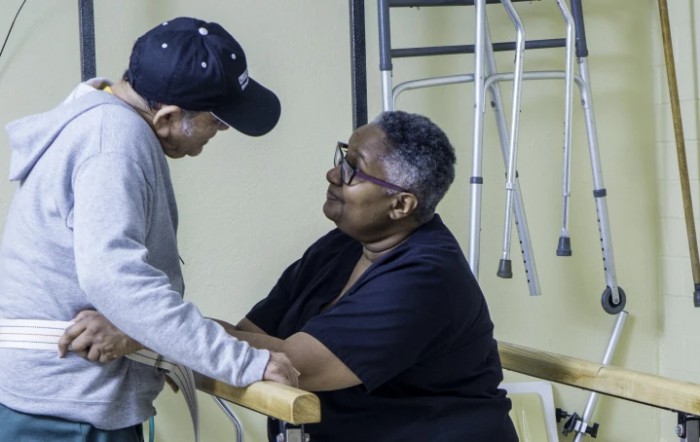 An elderly person receiving support during a physical therapy session.