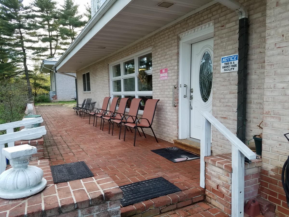 A cozy porch with multiple chairs lined up along a brick walkway.