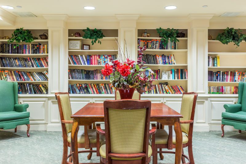 A cozy library reading space with a wooden table and chairs, surrounded by bookshelves filled with books.