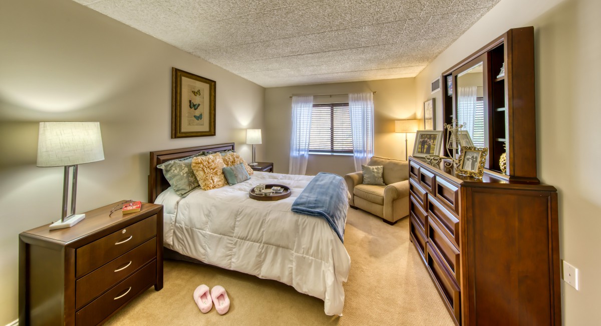 A cozy bedroom with a large bed, armchair, and warm lighting.