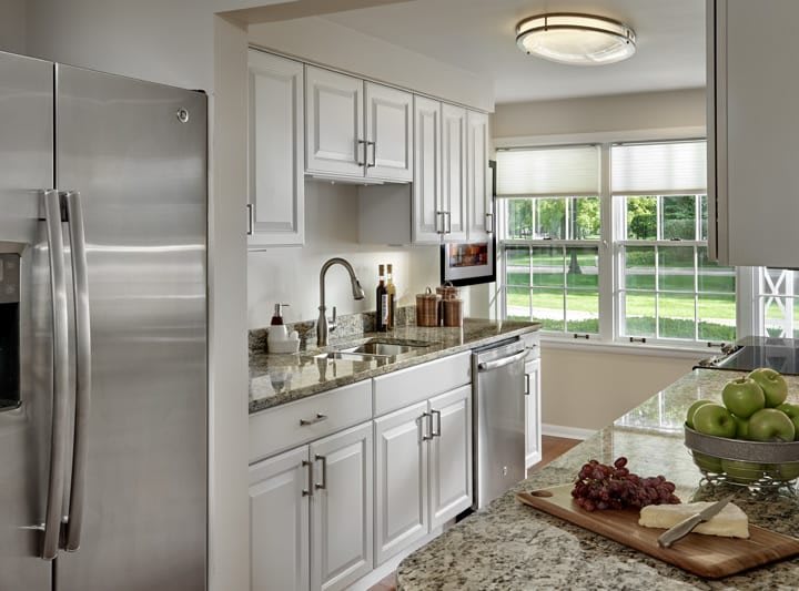 A modern kitchen with white cabinets, stainless steel appliances, and granite countertops, illuminated by natural light from large windows.