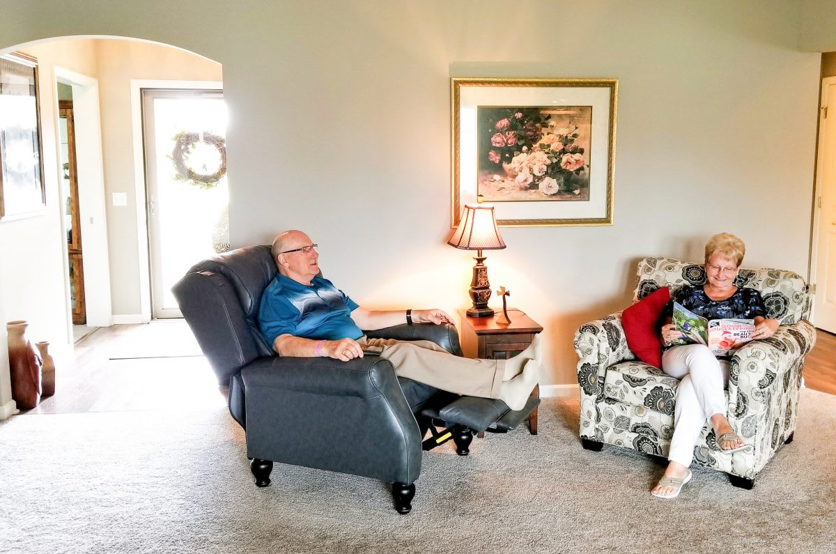 Two people relaxing in a comfortable living room setting, one seated in a recliner and the other on an armchair.