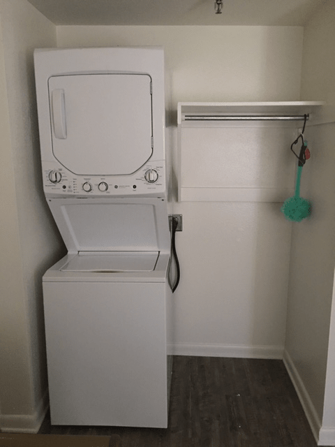 A compact laundry space with stacked washer and dryer units and an adjacent shelf.