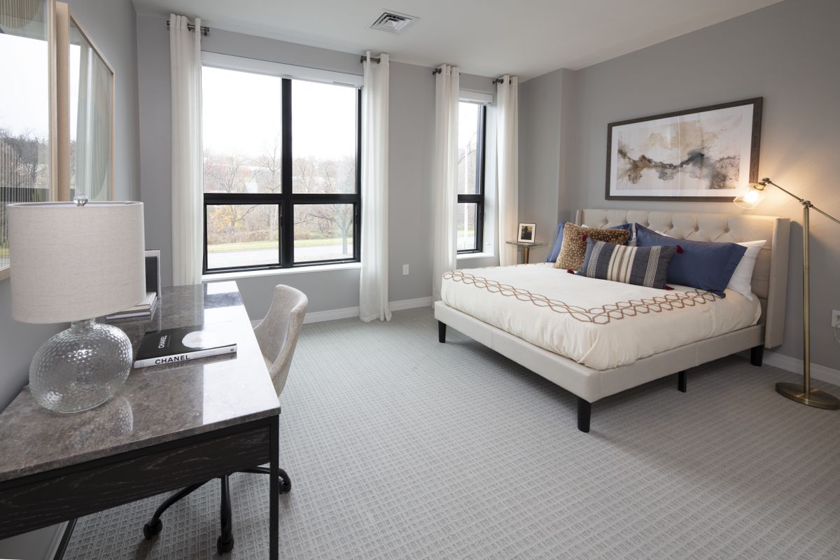 A modern bedroom with large windows, a comfortable bed, and a work desk.
