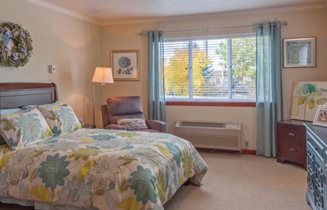 A cozy bedroom with a bed, chair, and large window allowing natural light.