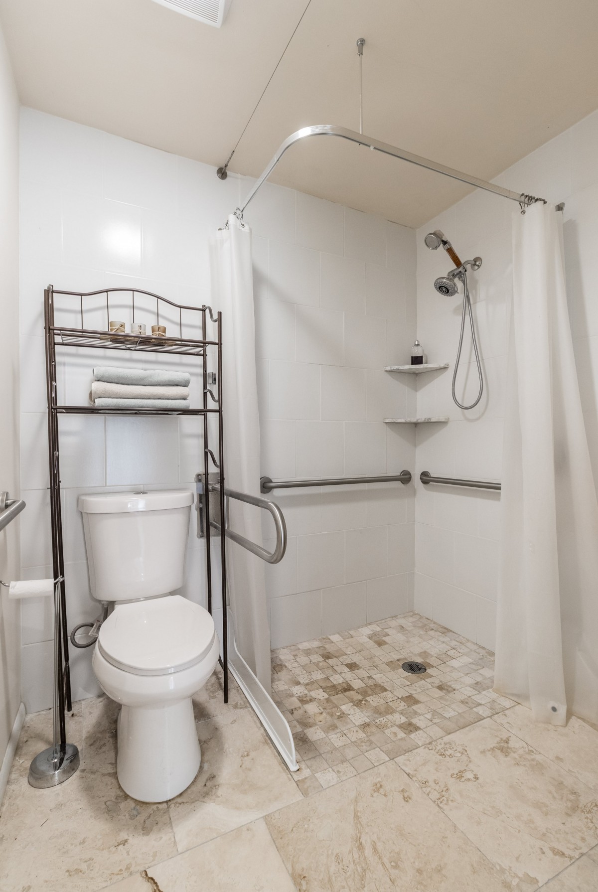 A bathroom with a toilet, shower area, and metal rack for towels.