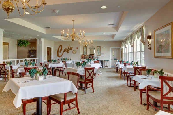 An elegant cafe interior with neatly arranged tables and chairs, featuring chandeliers and ample natural light.