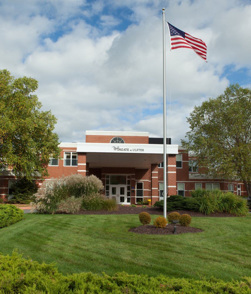 A building with an American flag surrounded by a well-maintained landscape of grass and trees under a cloudy sky.