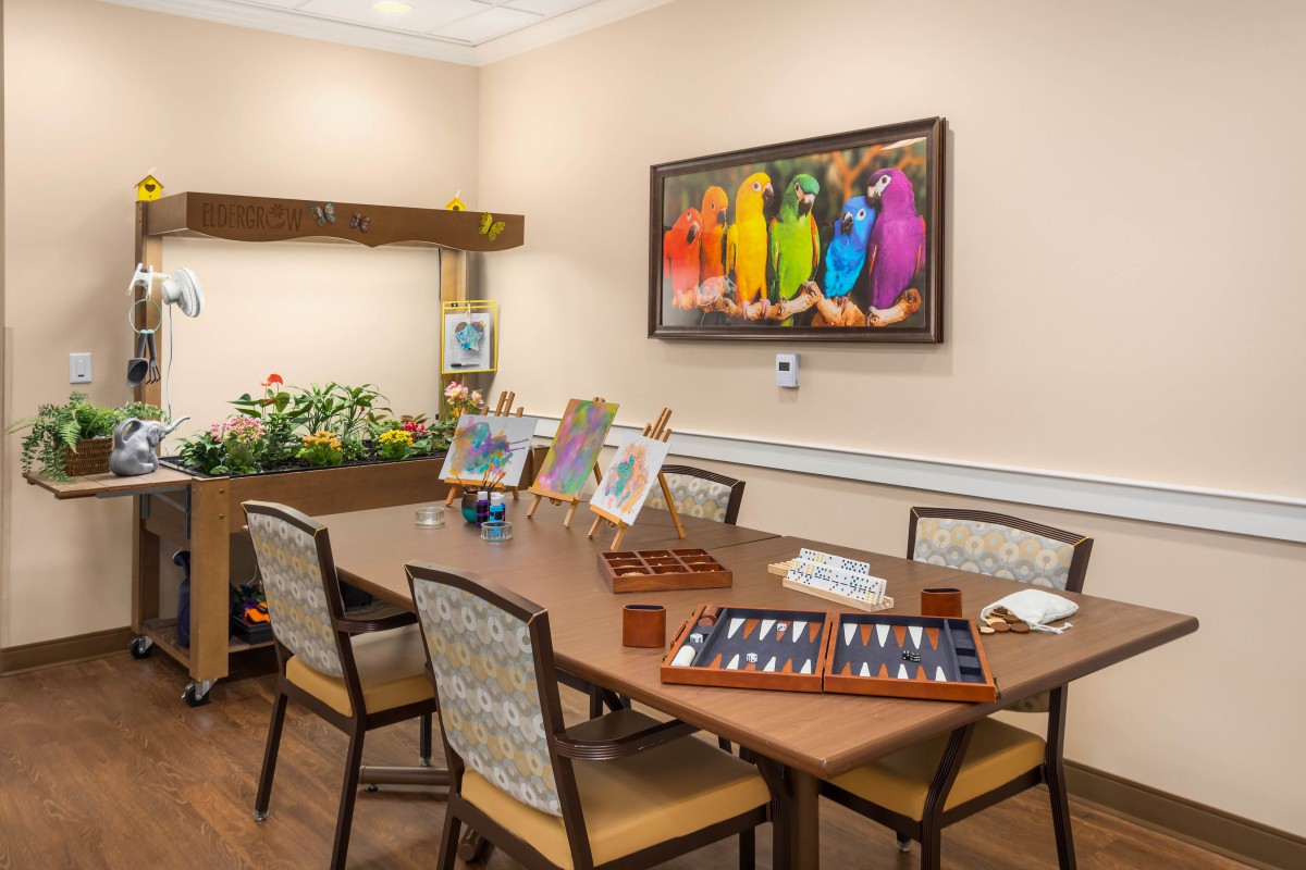 A creative art room with easels and painting supplies set up on a table, featuring a colorful bird painting on the wall.