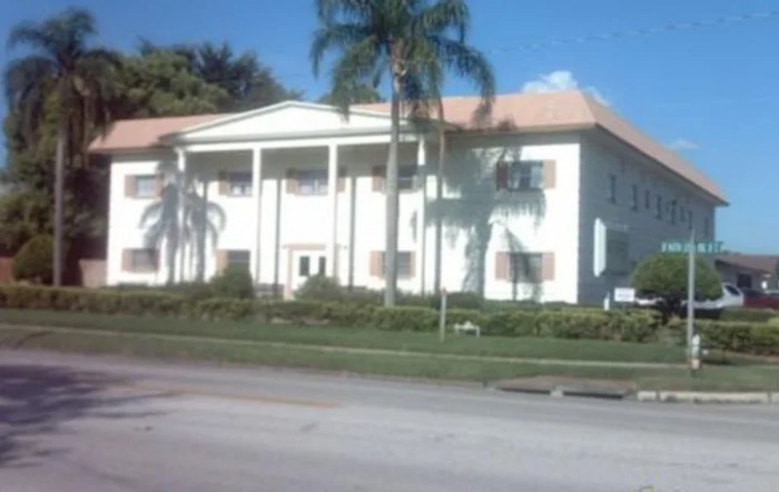 A sunny view of a building with columns and palm trees.