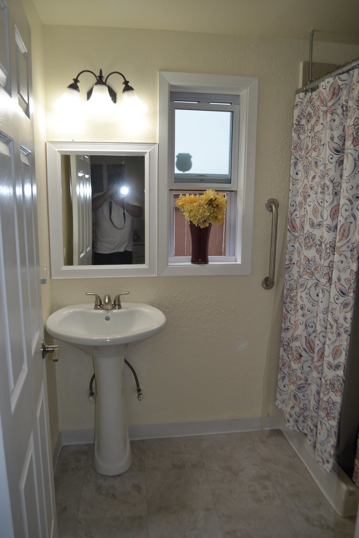 A small bathroom with a pedestal sink, mirror, and shower curtain.