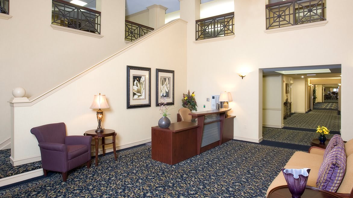 A hotel lobby with a reception desk, decorative lamps, and framed artwork on the walls.