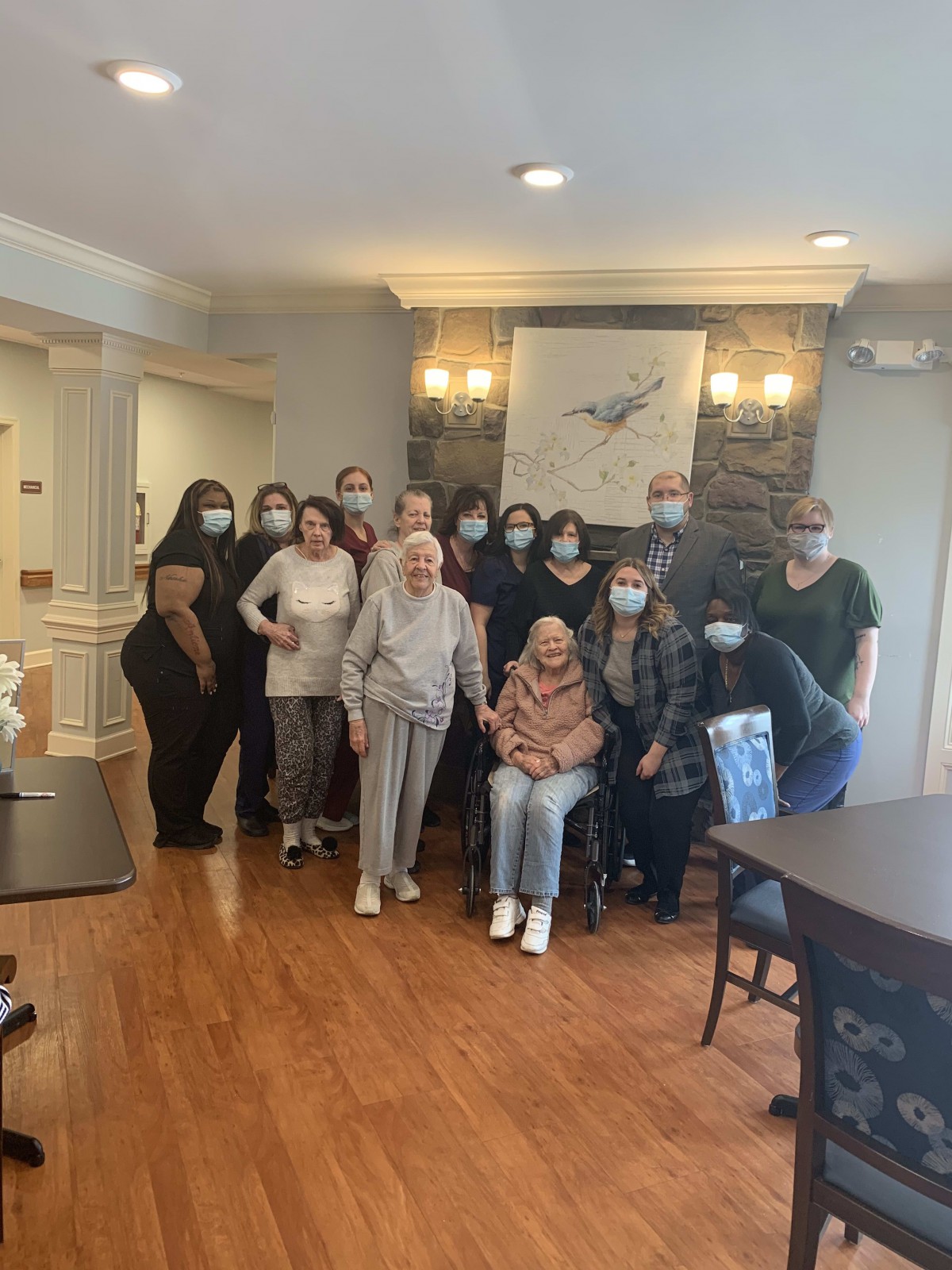 A group of people, including seniors and healthcare workers, gather for a photo indoors.
