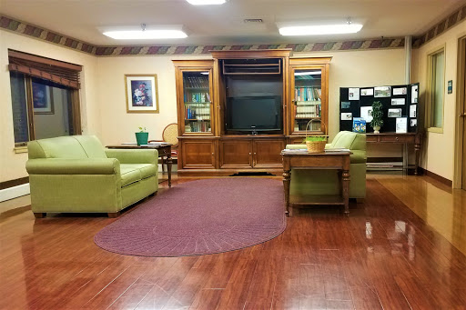 A cozy lounge area featuring green chairs, a television, and wooden cabinets.