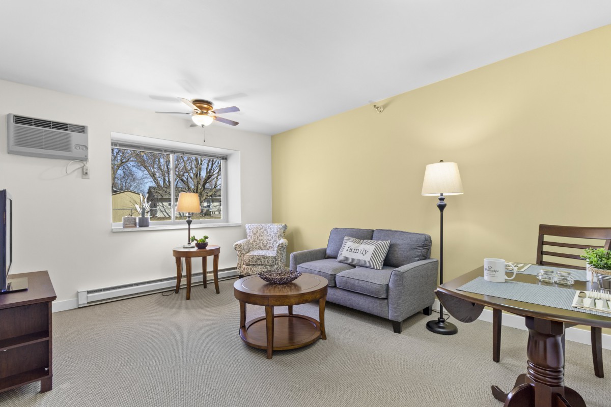 A cozy living room with a sofa, armchair, and coffee table, featuring soft lighting from a floor lamp.