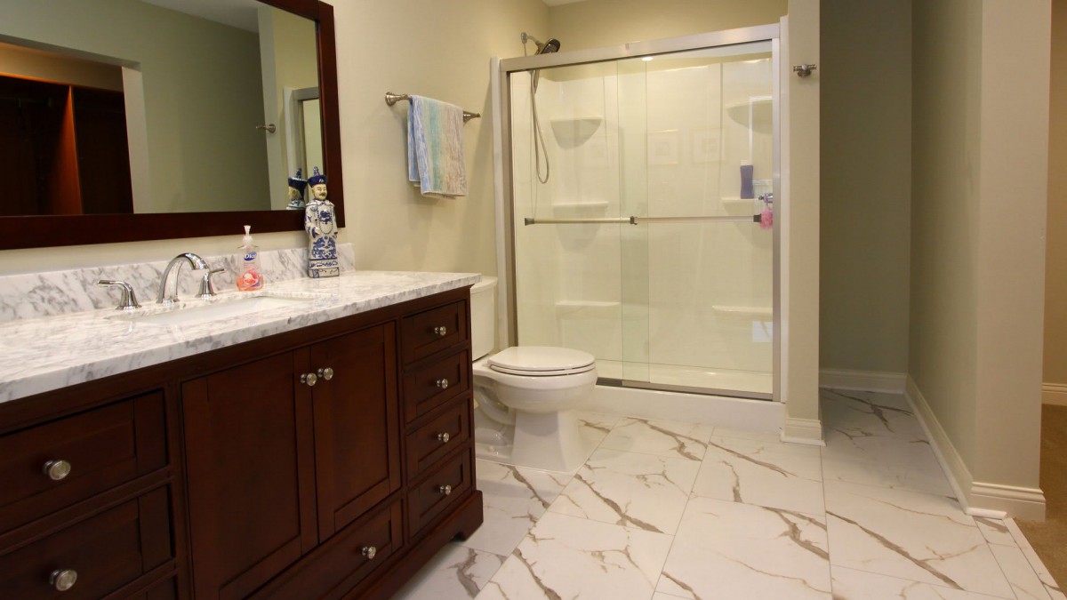 A modern bathroom with a marble floor, featuring a glass-enclosed shower, a toilet, and a wooden vanity with a mirror.