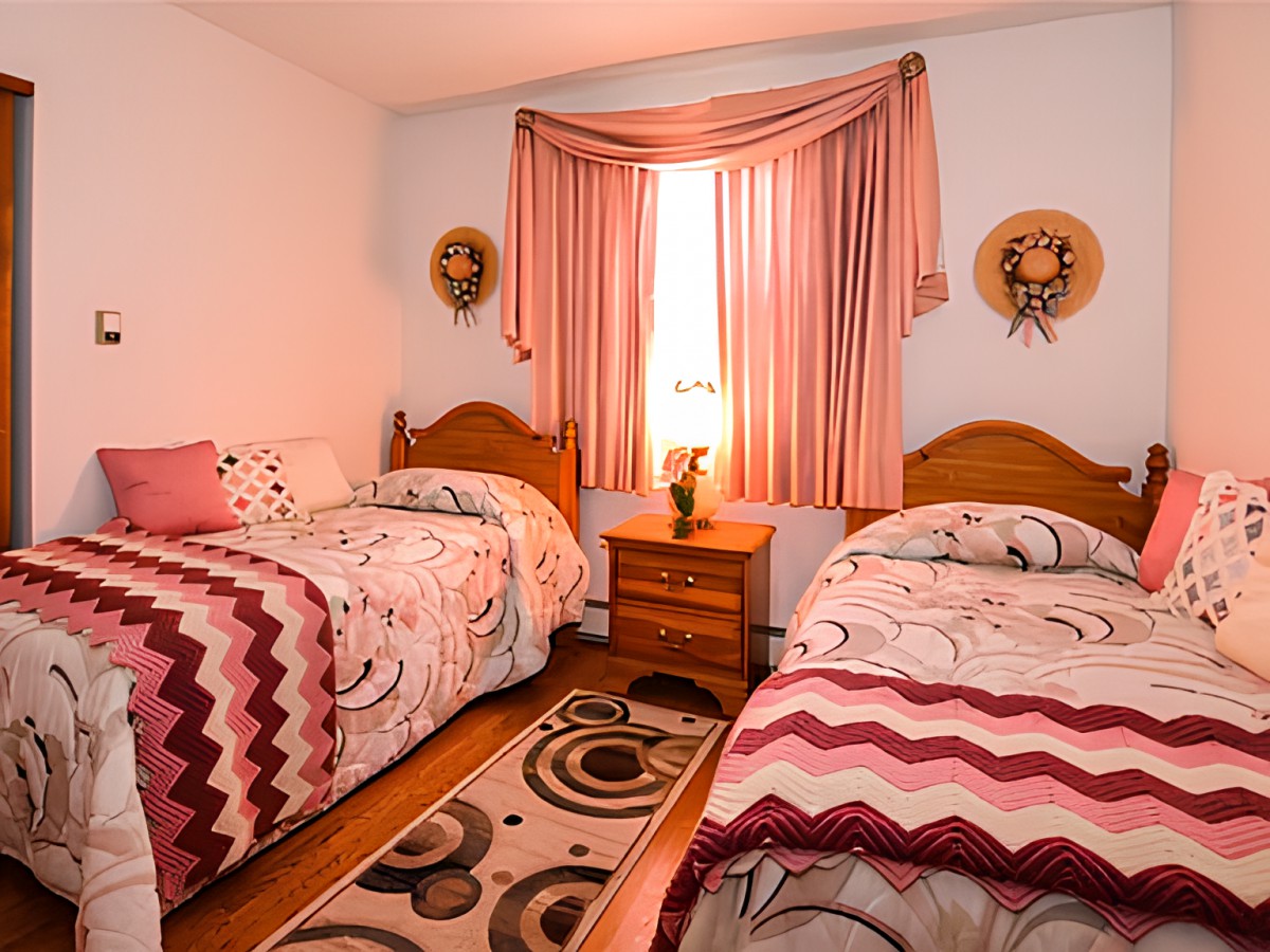 A cozy bedroom featuring twin beds with patterned bedspreads, a nightstand, and decorative curtains.