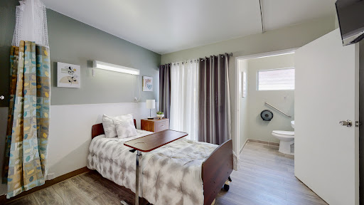 A well-lit hospital room featuring a single bed with a bedside table, curtains for privacy, and an en-suite bathroom.