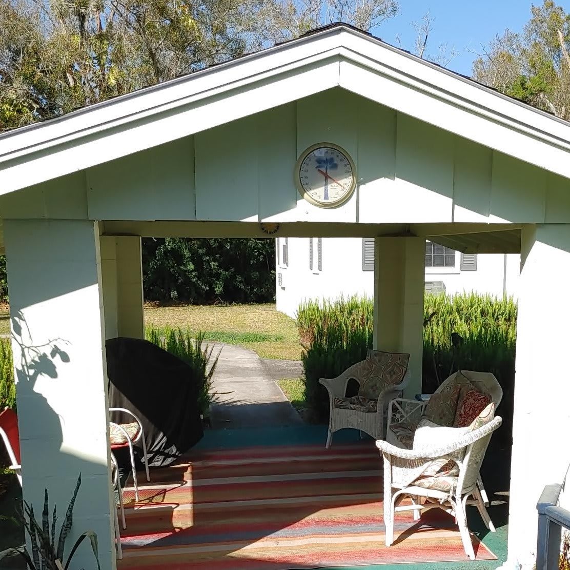 A cozy outdoor porch with chairs, surrounded by greenery on a sunny day.