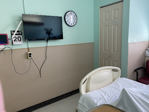 A patient room featuring a hospital bed, a television, and a wall clock.