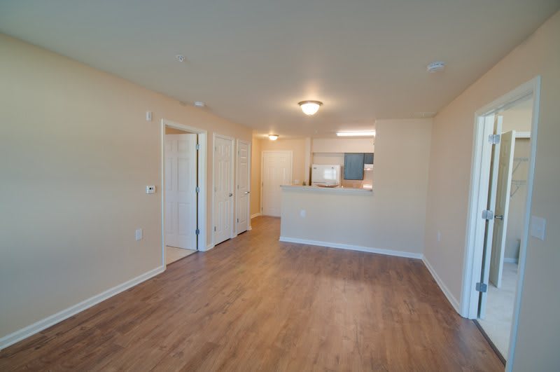 An empty apartment living room with hardwood floors and an open view into the kitchen.