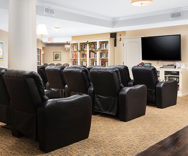 A cozy home theater setup with black recliner chairs and a large TV in front of bookshelves.