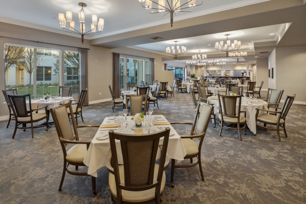 An elegant dining room with neatly arranged tables and chairs, featuring chandeliers and a spacious layout.