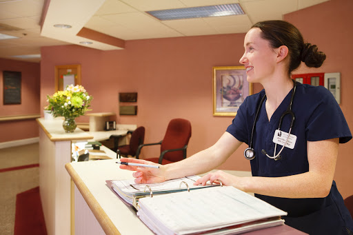 A nurse at the reception desk of a healthcare facility, assisting visitors.