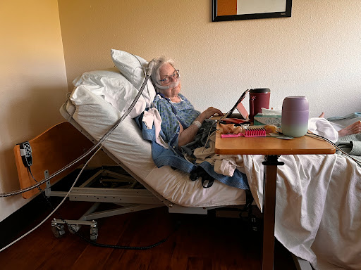 An elderly patient in a hospital room, seated in a hospital bed with medical equipment.