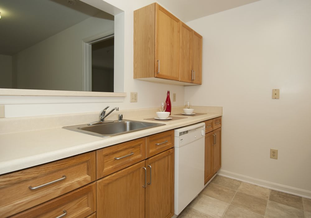 A clean and minimalist kitchen with wooden cabinets, a white countertop, a sink, and a dishwasher.