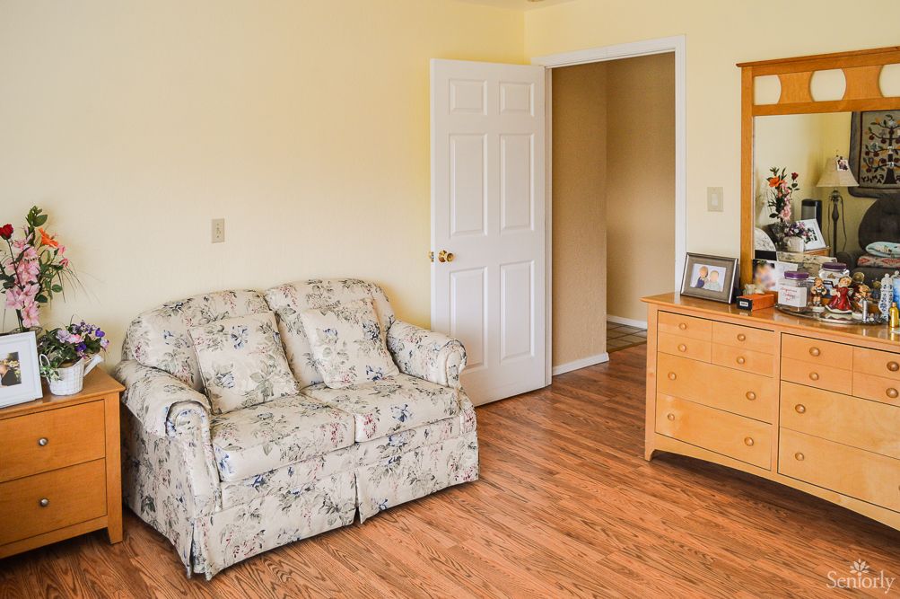 A cozy living room with a floral-patterned sofa, a wooden dresser, and an open door leading to another room.