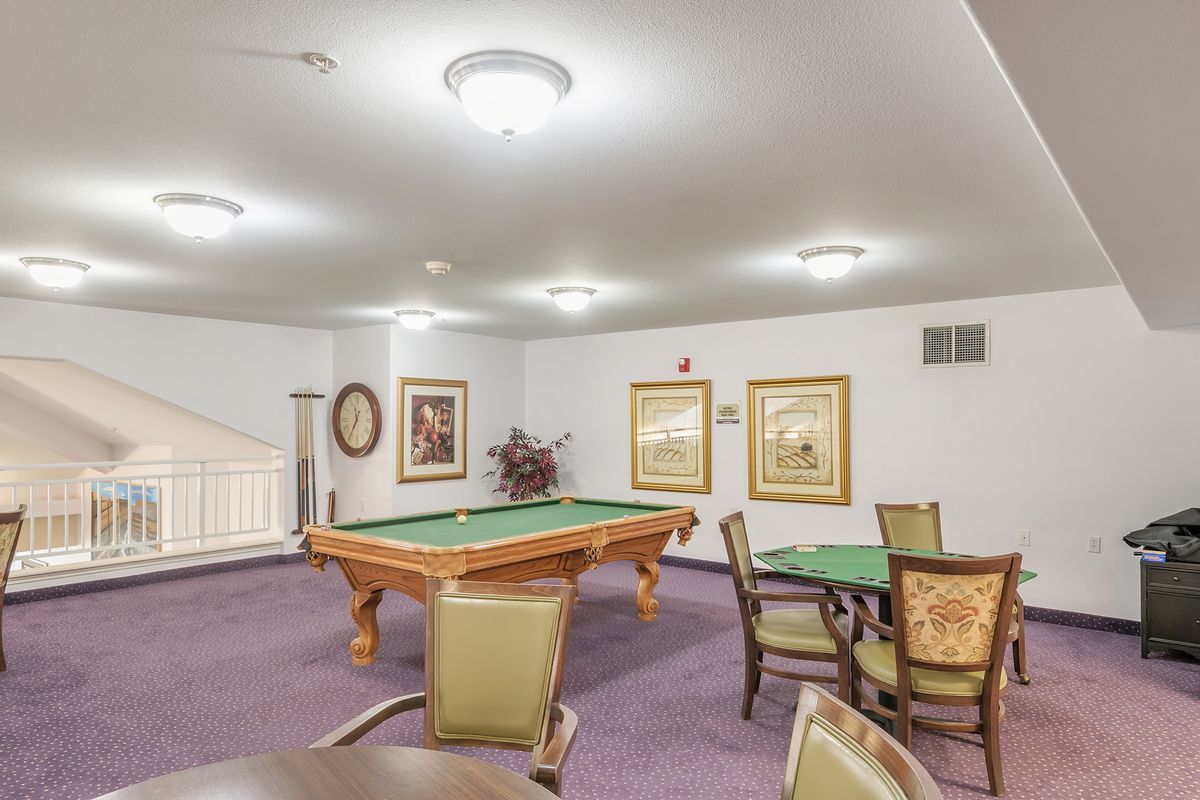 A well-lit game room featuring a pool table, chairs, and framed artwork on the walls.