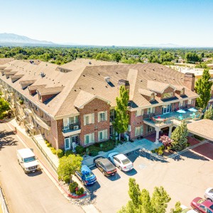 Aerial view of a large residential building with parked cars and surrounding greenery.