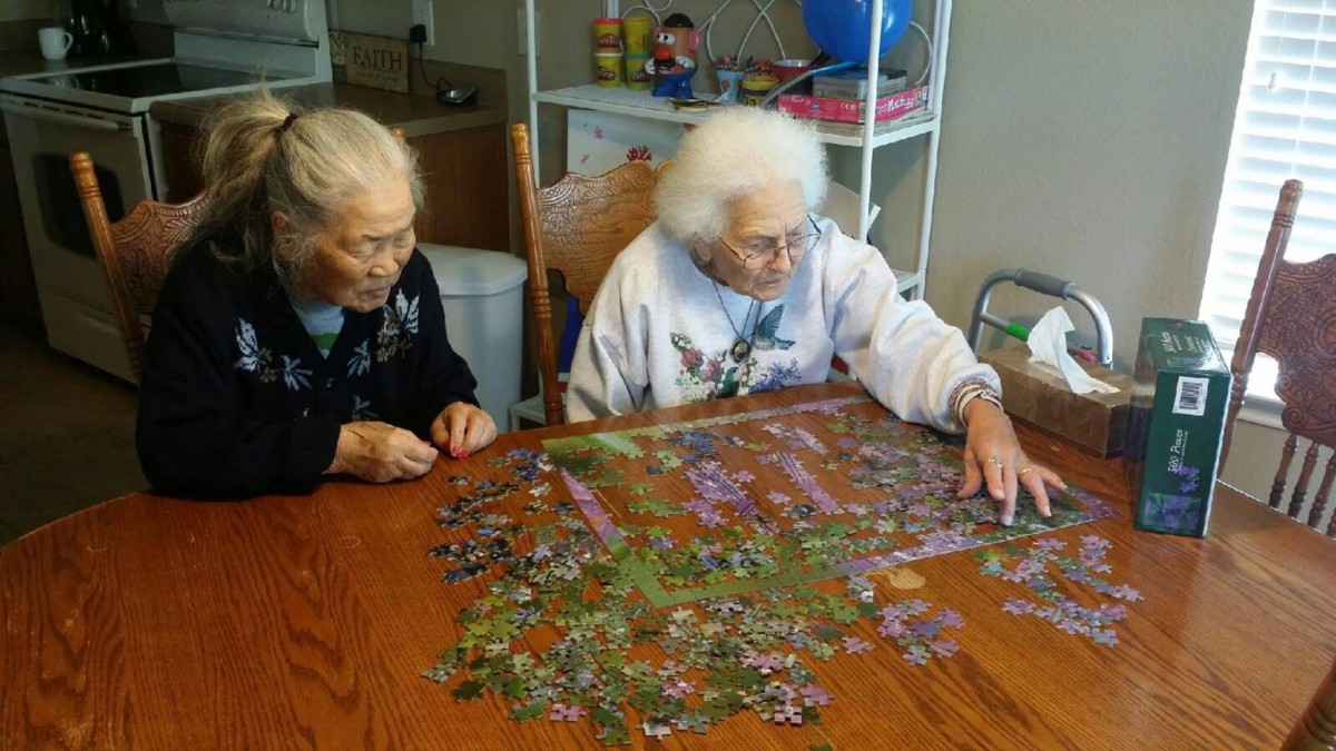 Two elderly individuals working on a jigsaw puzzle together at a table.