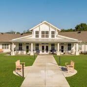 A charming building with a broad porch and well-manicured lawn, featuring benches along a concrete pathway.
