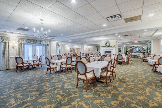 A spacious and elegant restaurant dining room with neatly arranged tables and chairs, featuring a chandelier and carpeted flooring.
