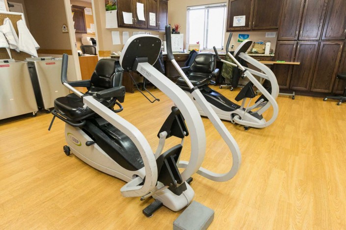 A fitness center with elliptical machines lined up on a wooden floor.