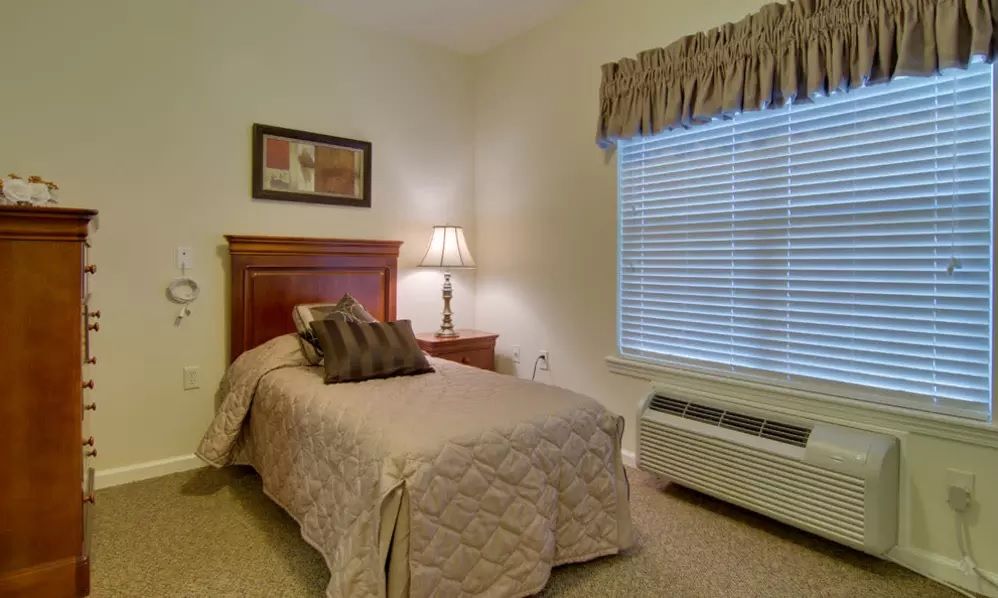 A cozy bedroom with a single bed, a lamp on a bedside table, and a window with curtains.